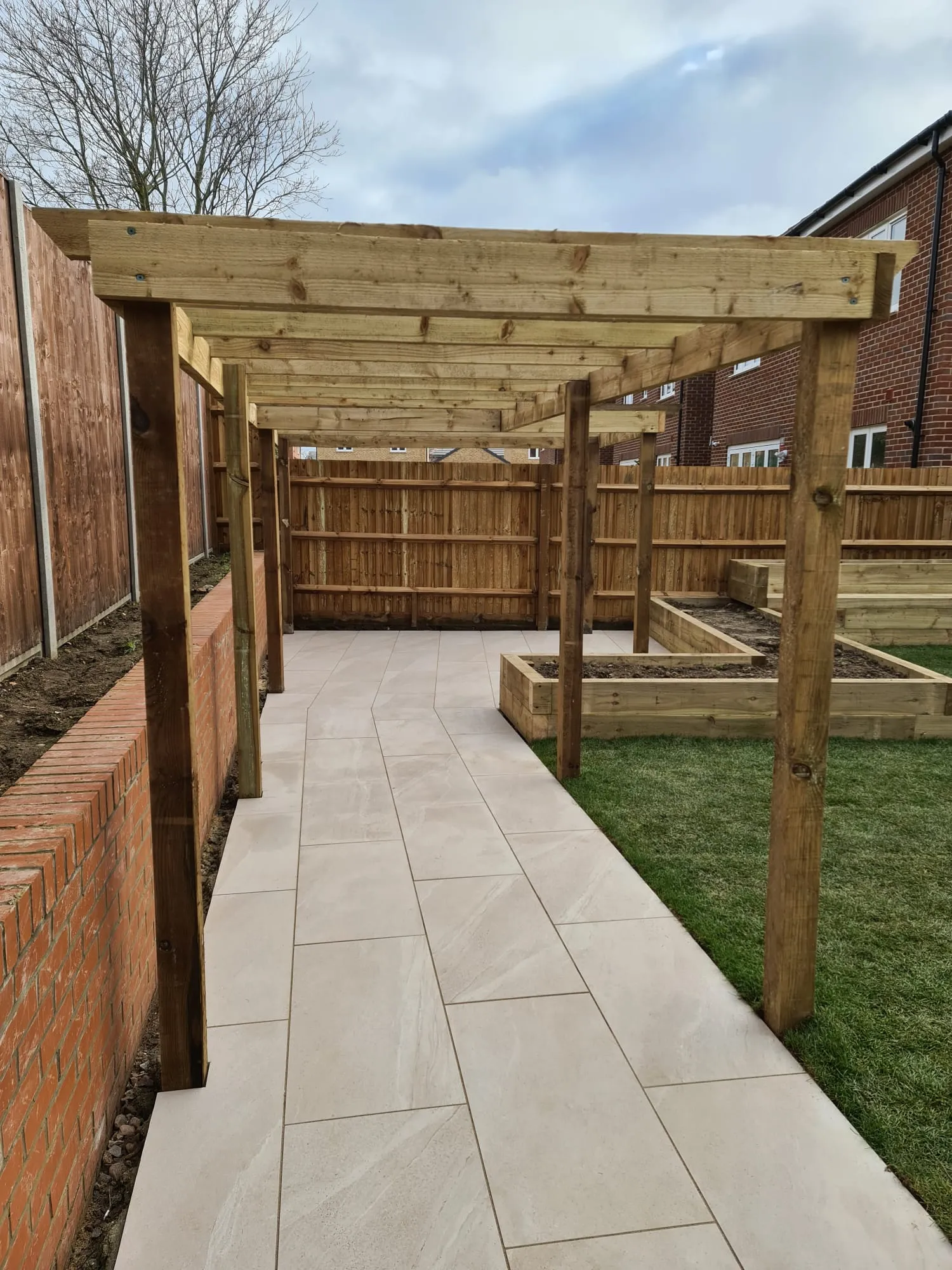 A patio area with a wooden pergolan and a brick wall.